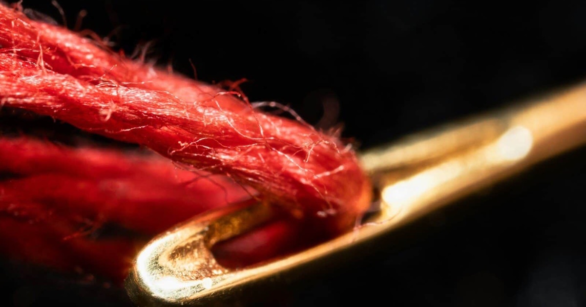 Red thread passing through the eye of a golden needle, symbol for the red thread in your career
